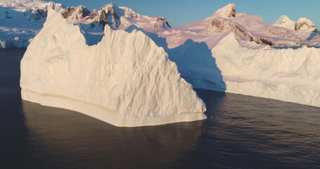 Wall Mural - Huge iceberg floats Antarctic waters in sunset light, aerial drone footage. Breathtaking scene of Antarctica glacier ice wall, mountains in background. Cinematic ecology scene. Zoom out panorama