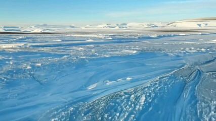 Sticker - A large, empty, snow-covered field with a blue sky in the background. The sky is clear and bright, and the snow is white and powdery. The scene is peaceful and serene, with no signs of human activity