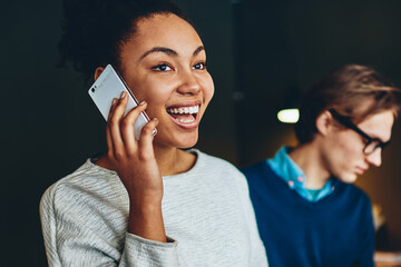 Cheerful young african american woman excites with getting good news during telephone conversation while her male colleague read report in office, smiling female satisfied with operator consultancy