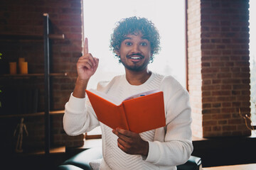 Sticker - Photo of excited good mood guy wear white sweatshirt pointing finger up reading book having rest indoors room home house