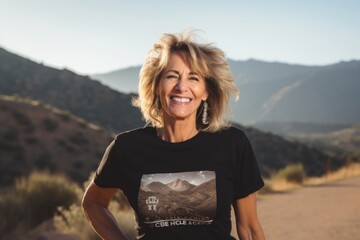 Sticker - Portrait of a smiling woman in her 50s sporting a vintage band t-shirt isolated on backdrop of mountain peaks