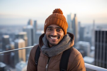 Canvas Print - Portrait of a happy indian man in his 30s dressed in a warm ski hat isolated on stunning skyscraper skyline