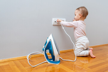 A baby dangerously holds the electrical cord of a switched-on iron.