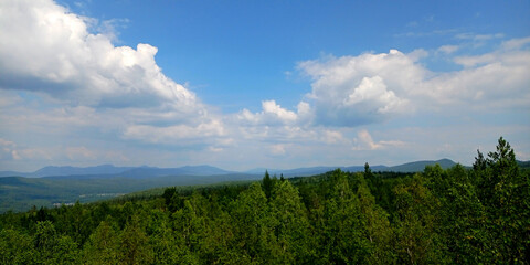 Photos of nature. Traveling through the forest.  Taganai National Park, Russia. landscape with a valley in the fog behind the forest on a grassy hill. fluffy clouds on a bright blue sky