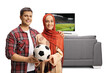 © Ljupco Smokovski - Young man and a woman wearing a hijab holding a football in front of tv