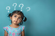 © PRASANNAPIX - A little Indian Gorgious girl thinking with question marks floating above her head on a light blue background