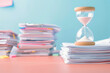 © Sunday Cat Studio - A stack of documents beside an hourglass symbolizes time management and the importance of organization in workspaces.
