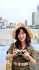 Wall Mural - Young Asian woman backpack traveler using a camera in express boat pier on Chao Phraya River in Bangkok. Journey trip lifestyle, world travel explorer or Asia tourism concept. Vertical footage.