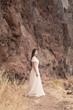 © Milou Dirks - Art portrait of young asian woman in classic white dress standing near red rough wall of cliff near ocean on Madeira