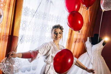 A woman is holding a bunch of red balloons and smiling. The balloons are scattered around her, creating a festive atmosphere. The scene suggests a celebration or a special event