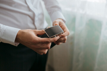 A man is holding a belt in his hand. The belt is black and has a silver buckle. The man is wearing a white shirt and black pants. Concept of formality and professionalism