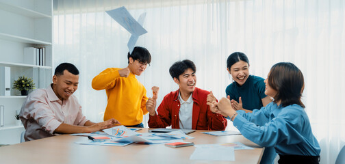 Excited and happy startup company employee celebrate and throw paper in the air after make successful business. Teamwork and positive environemtn create productive and supportive workplace. Synergic