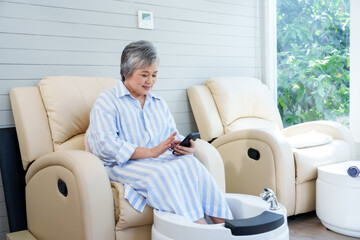 Poster - Elderly spa customer sits comfortably, engaging with smartphone while waiting for service. Woman in striped dress exemplifies relaxation, modern convenience, serene anticipation in small business spa.