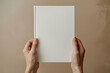 © Sebelas Studio - A person holding up an empty white book with a plain cover, showing the blank page for writing space and text on a beige background
