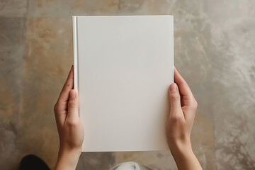 Wall Mural - A person holding up an empty white book with a plain cover, showing the blank page for writing space and text on a beige background