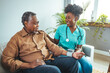 © Dragana Gordic - A professional black mid-adult female nurse, in scrubs, attentively checks the blood pressure of an elderly black male sitting comfortably in his home.