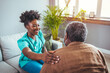 © Dragana Gordic - A mid-adult Black nurse in scrubs engages with an elderly man in a home setting, providing attentive healthcare assistance with warmth and professionalism