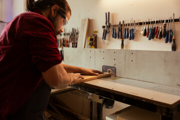 Wall Mural - Woodworker wearing safety glasses operating spindle moulder to create bespoke joinery for client commissioned project. Manufacturer performing tasks on wood shaper, shaping and cutting planks