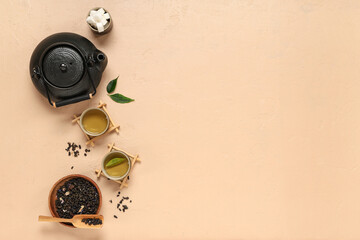 Wall Mural - Teapot with cups, wooden bowl of dry tea and sugar on beige background