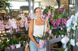 © JackF - Girl in sales area of flower exhibition examines orchid flower, chooses plants for landscaping apartment, front garden. Exhibition and sale, self-service store with plants and related products