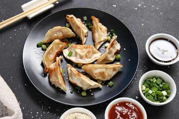 Plate with fried Japanese gyoza and bowls of sauces on black background