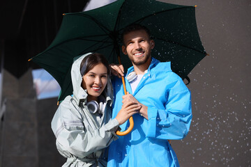 Sticker - Happy young couple in raincoats holding umbrella on rainy day outdoors