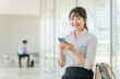 © buritora - オフィスビルでスマホを使う若いアジア人ビジネスウーマン