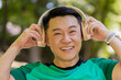 © Andrii Iemelianenko - Happy young Japanese man put on wireless modern headphones earphones. Runner jogger guy sport male run running in park outdoors enjoy music listening song audio jogging healthy lifestyle fitness.