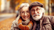 © bluecreamy - Elderly happy senior couple with a smile, smiling at the camera. The woman with a coat and an orange scarf, the man with a white beard, is wearing a brown jacket. autumn leaves in golden hues