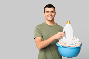 Poster - Young man with clean towels in basin and bottle of detergent on grey background