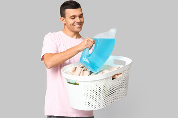 Poster - Young man with laundry basket and bottle of detergent on grey background