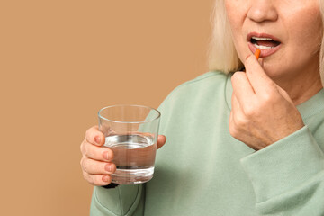 Canvas Print - Beautiful mature woman with pill and glass of water on brown background