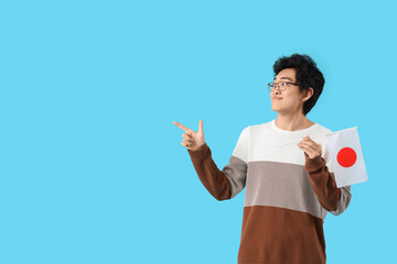 Sticker - Young Asian man with flag of Japan pointing at something on blue background