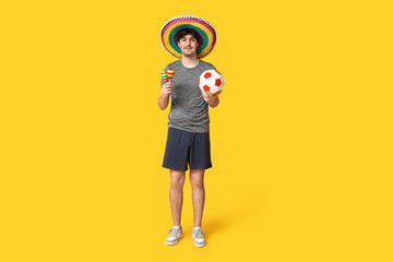 Wall Mural - Young male football player with sombrero, soccer ball and maracas on yellow background