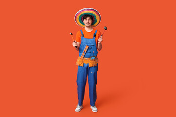 Wall Mural - Young male construction worker with sombrero and tools on orange background