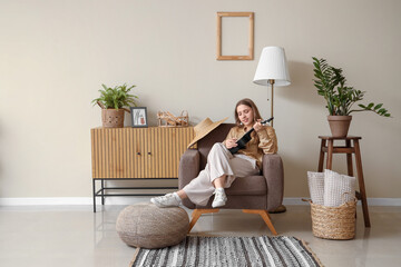 Canvas Print - Beautiful young woman playing ukulele while sitting in armchair in living room