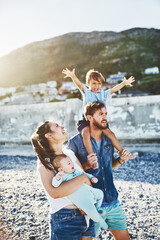 Piggyback, parents or children at beach for walking, holiday or travel in Portugal with boy, baby or family. Happy, mom or father with infant at sea on vacation together for love or playing to relax