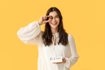 Wall Mural - Young woman with box of delicious chocolate candies on yellow background