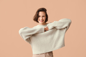 Poster - Happy young woman in stylish grey sweater on brown background