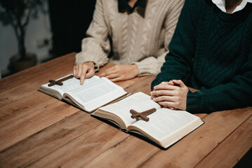 Wall Mural - Group of Christians sit together and pray around a wooden table with blurred open Bible pages in their homeroom.