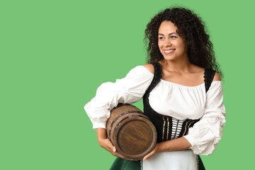 Happy African-American woman with barrel of beer on green background. Octoberfest celebration