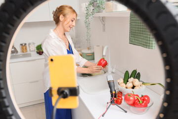 Wall Mural - Mature woman washing bell pepper while recording cooking video class in kitchen