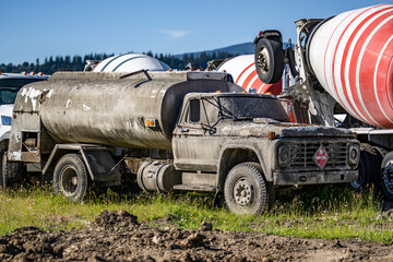 An old vintage semi truck with a tank trailer used to transport concrete mix for many years is now resting on an industrial parking lot