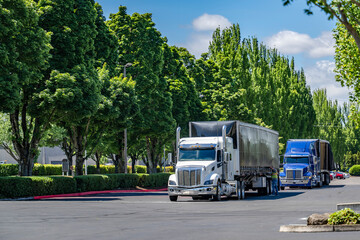 Wall Mural - Team of two big rig semi trucks with tented Conestoga flat bed semi trailers loading cargo standing on the warehouse parking lot