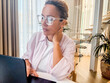 © simona - Focused middle aged woman holding document and using laptop at home. Female adult worker checking life insurance or savings financial account, paying bill on bank online app, planning budget