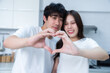 © Thinapob - Happy portrait of loving young asian of having fun standing a cheerful heart shaped hands  preparing food and enjoy cook cooking bread while standing on a kitchen Condo life or home