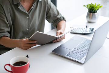 Wall Mural - Businesswoman sitting at desk on couch in workplace or at home working on laptop and analyzing data on charts and graphs and writing on papers to make business plan and strategies for company, 