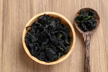 Wall Mural - Dried Wakame seaweed or sea mustard in bowl and spoon on wooden background, Table top view