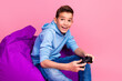 © deagreez - Photo portrait of cute teen boy beanbag hold joystick play videogame dressed stylish blue clothes isolated on pink color background