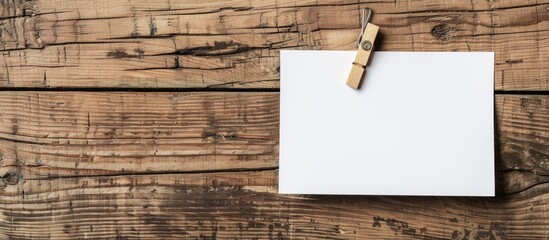 Aufkleber - A clothespin is clipped onto a blank paper against a wooden backdrop offering a suitable copy space image